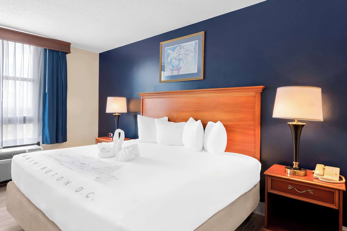 A hotel room with a large bed, two bedside lamps, a nightstand with a telephone, and a framed picture on the wall.