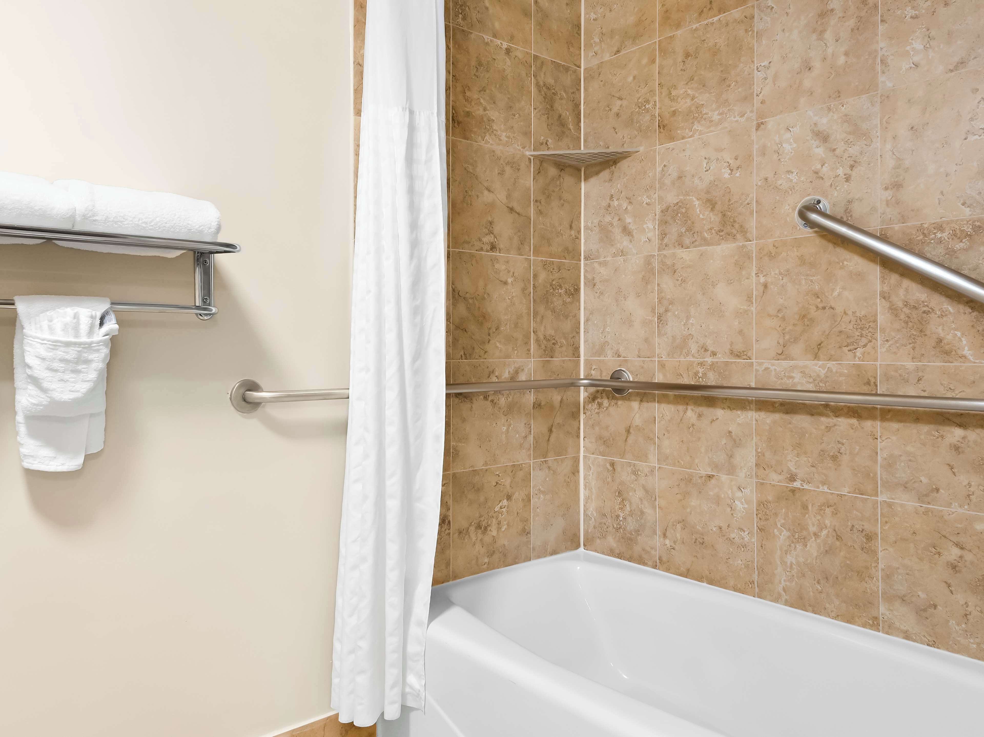 A bathroom with a bathtub, a shower with a grab bar, and a towel rack with towels.