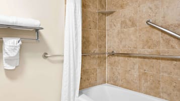 A bathroom with a bathtub, a shower with a grab bar, and a towel rack with towels.