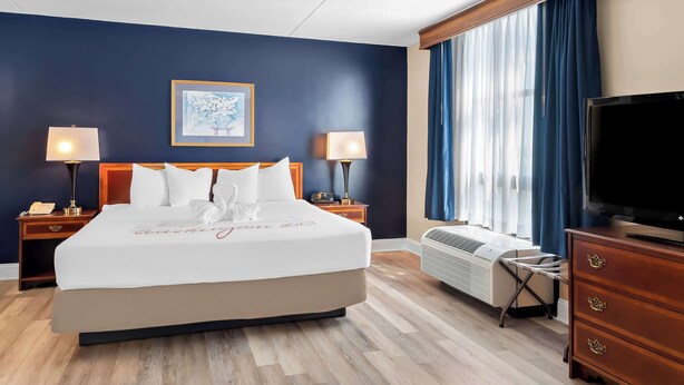 A hotel room with a large bed, two bedside lamps, a flat-screen TV, a dresser, and a window with curtains. - Best Western Potomac Mills (Woodbridge)