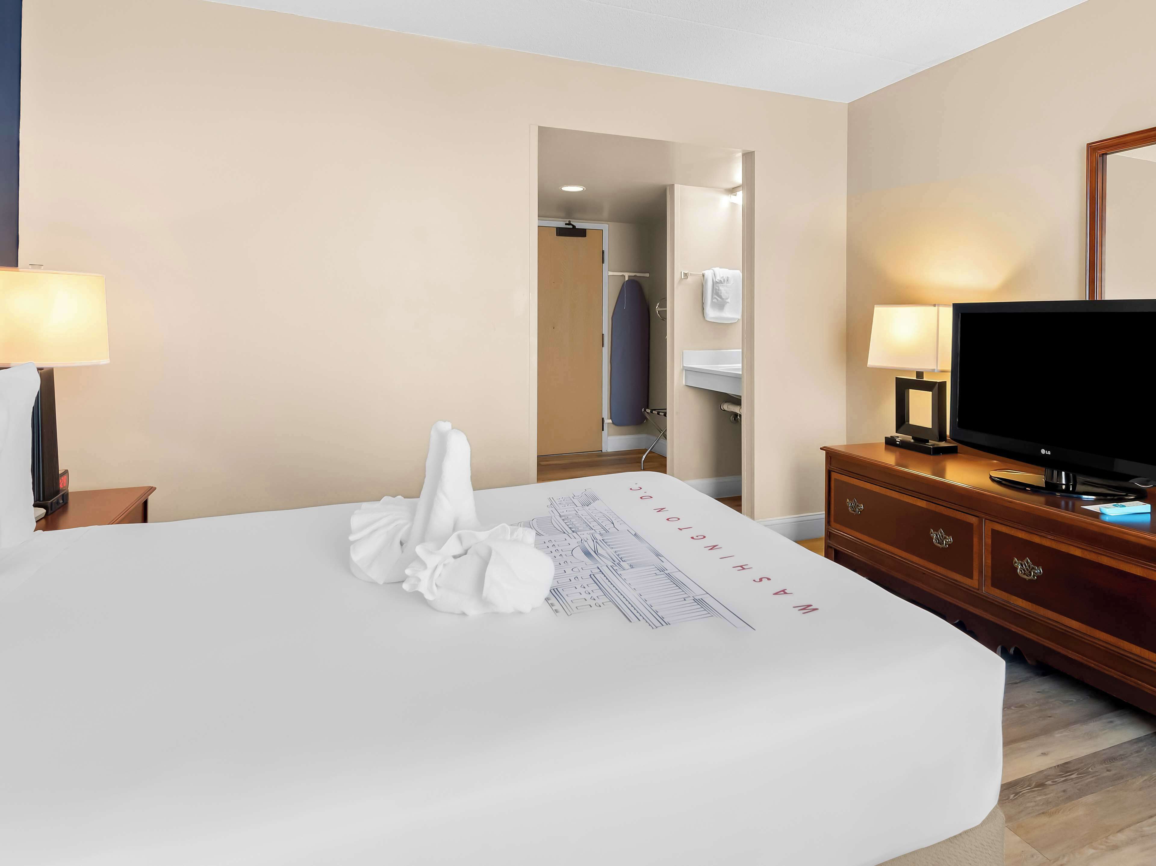 A hotel room with a bed, a television, a dresser, a mirror, and a bathroom visible through an open door.