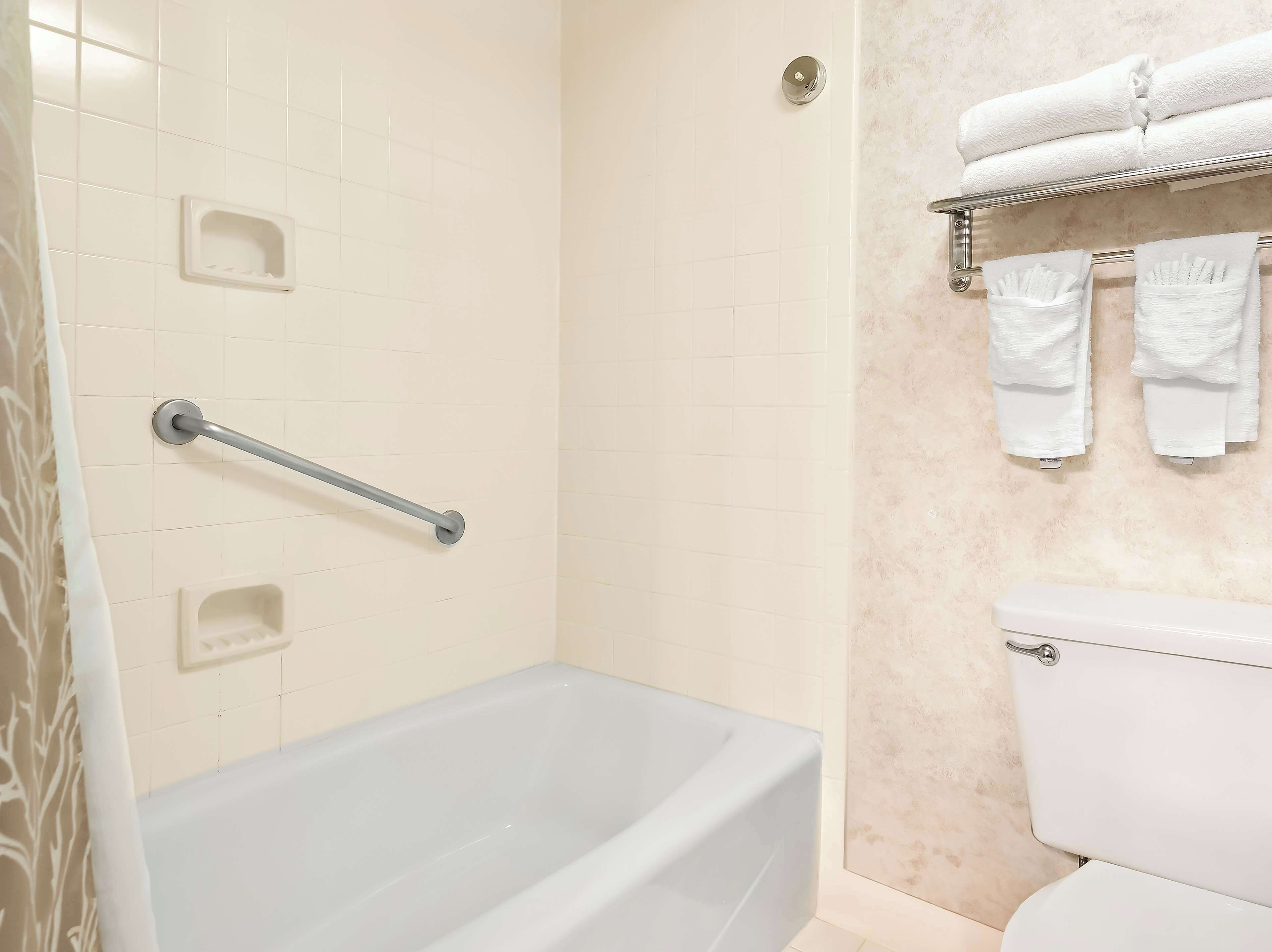 Un baño con bañera, inodoro, barra de apoyo y toallero con toallas.
