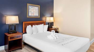 A hotel room with a bed, two bedside lamps, a nightstand, a framed picture on the wall, and a white swan decoration on the bed.