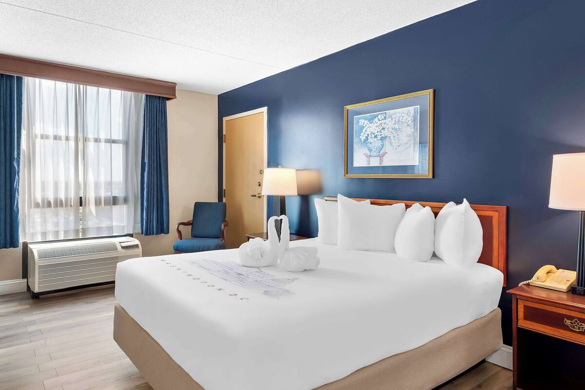 A hotel room with a large bed, a desk, a chair, a lamp, and a painting on the wall.