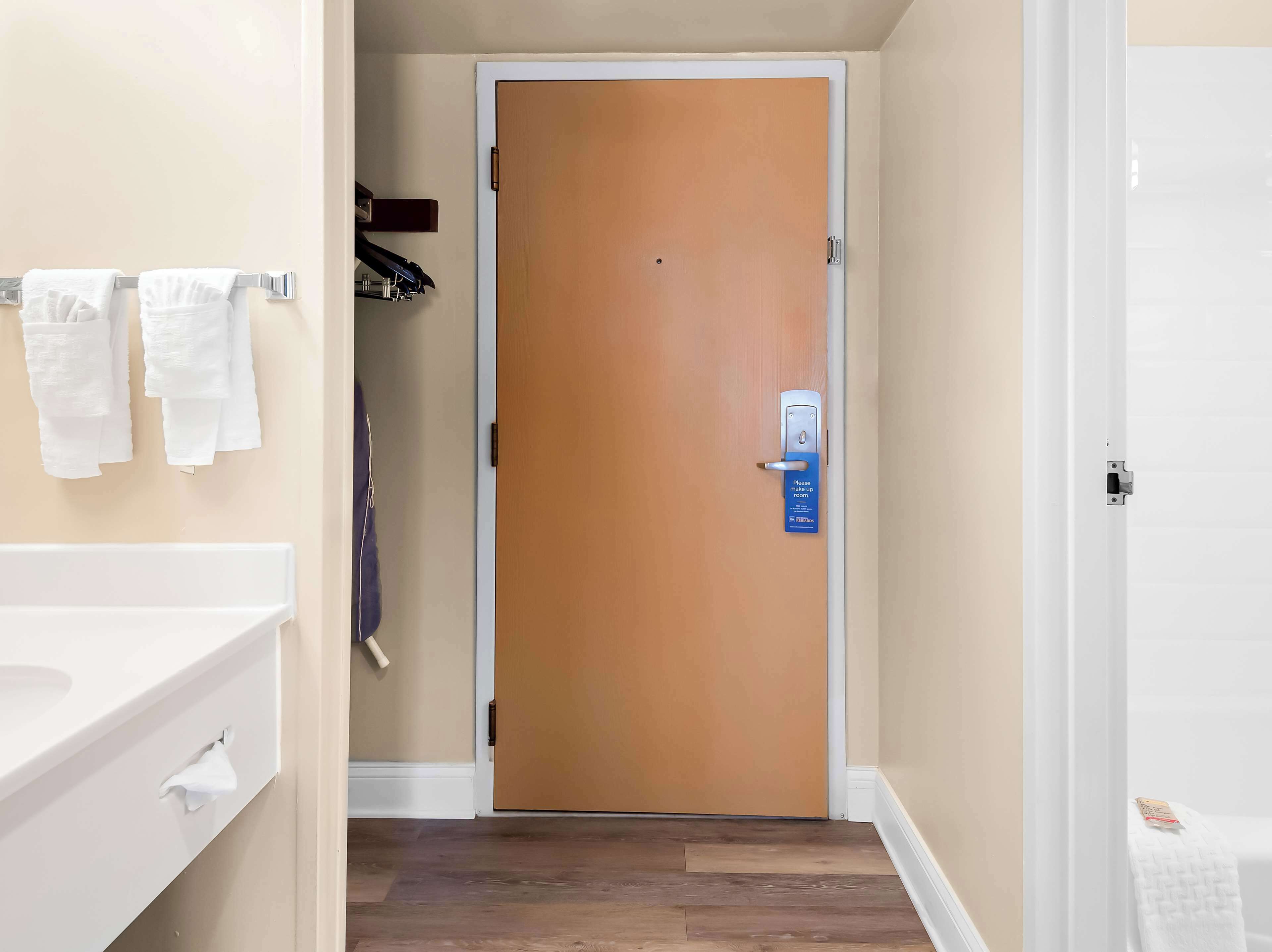 Un baño con un lavamanos blanco, un perchero con toallas y una puerta de madera con un letrero azul.