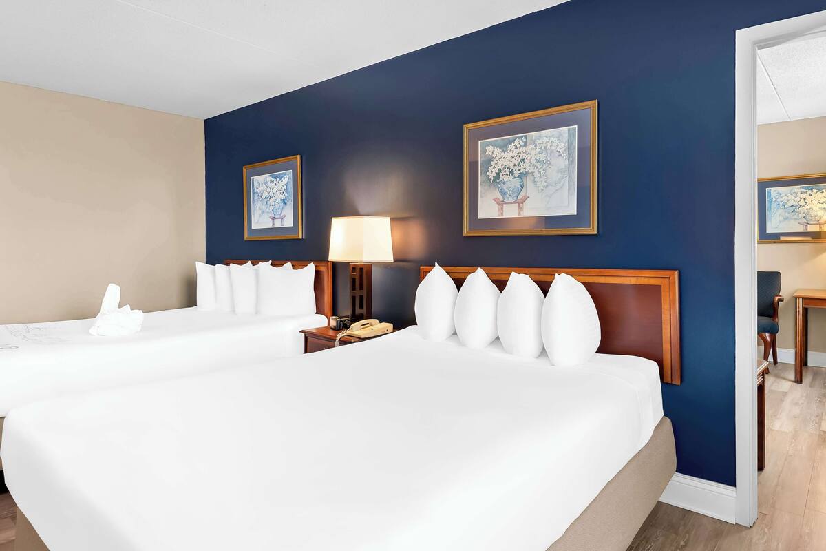 A hotel room with two beds, a nightstand, a lamp, and two framed artworks on the wall.