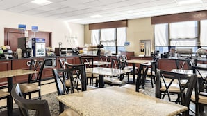 A hotel dining area with multiple tables and chairs, a coffee machine, and a counter with food items. - Best Western Potomac Mills (Woodbridge)