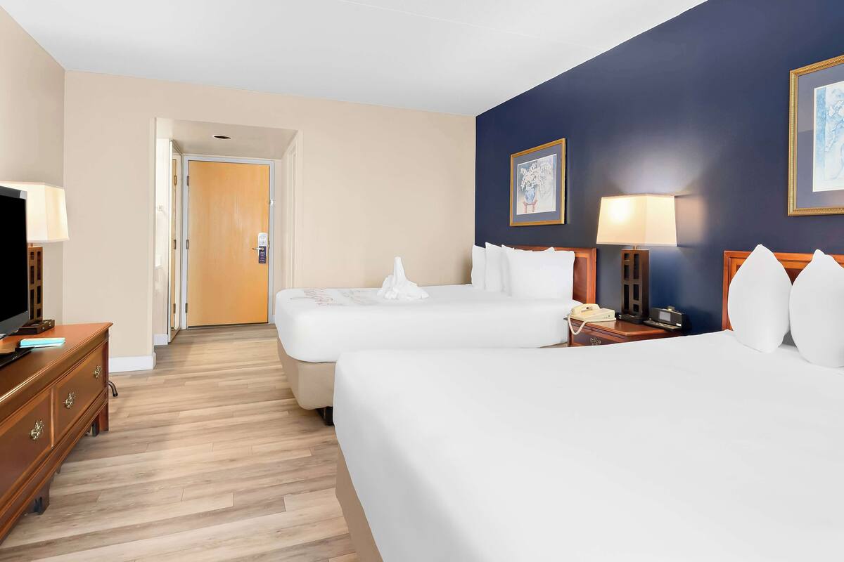 A hotel room with two beds, a television, a desk, and a door leading to another room.