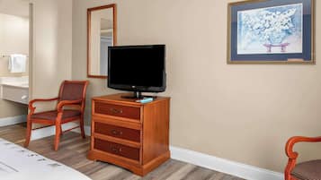 A hotel room with a wooden dresser, a television, a chair, a mirror, and a framed picture on the wall.