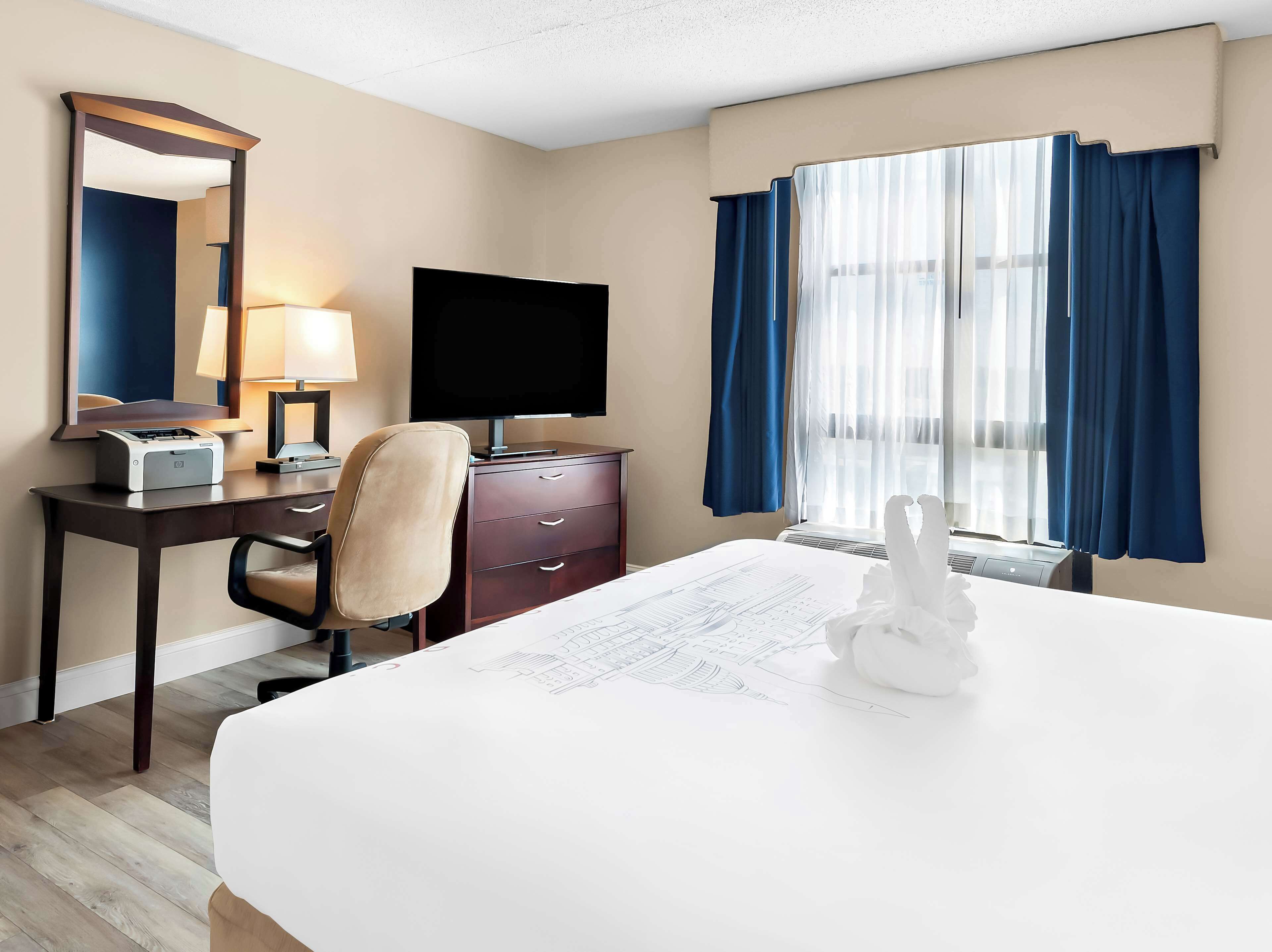 A hotel room with a bed, desk, chair, TV, and a window with curtains.