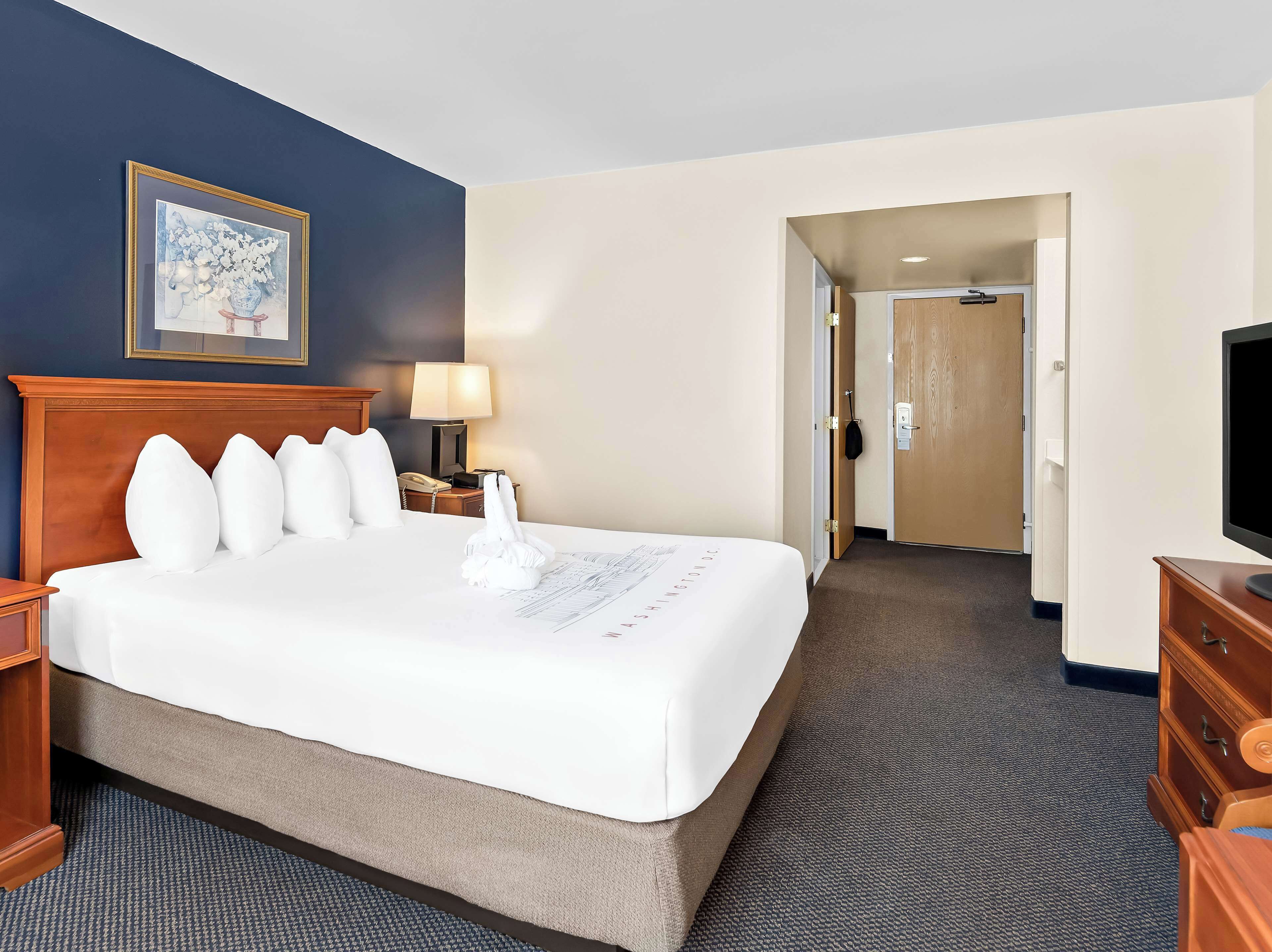 A hotel room with a large bed, a bedside lamp, a telephone, a TV, and a painting on the wall.