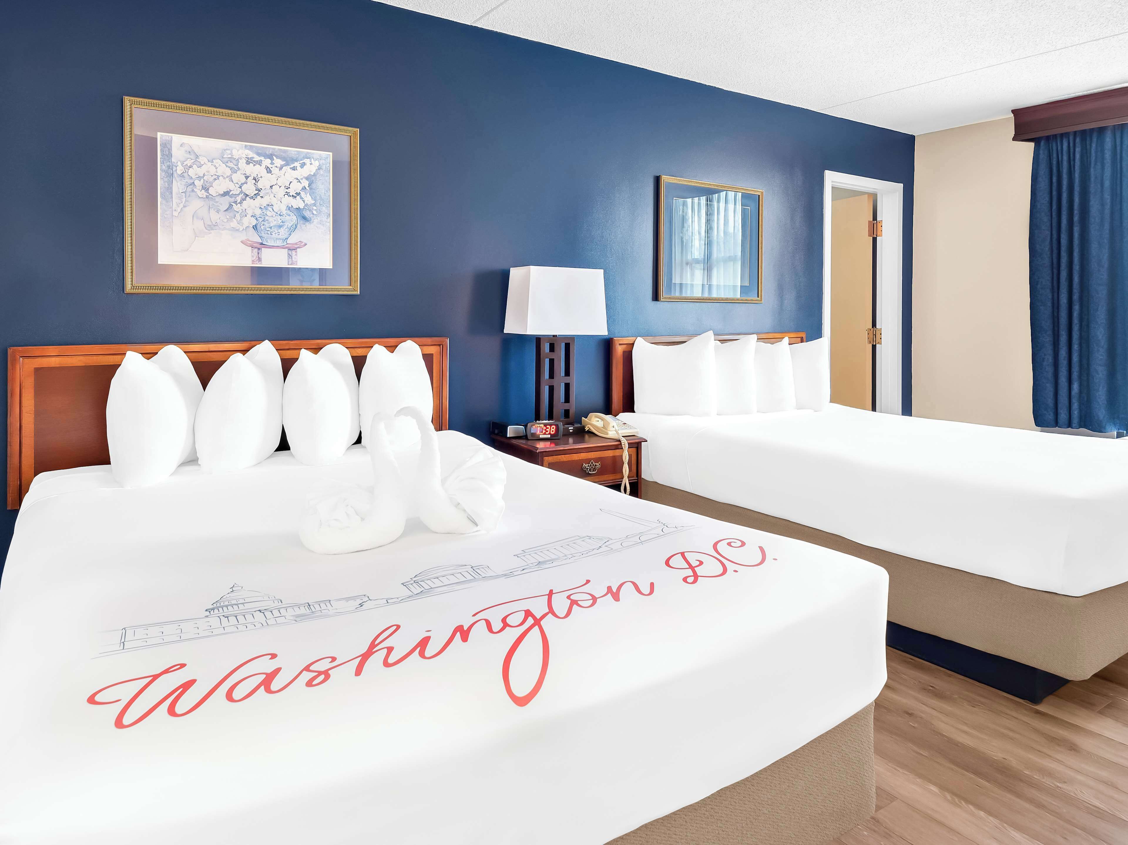 A hotel room with two beds, a nightstand with a lamp, a framed picture on the wall, and a door with a curtain.