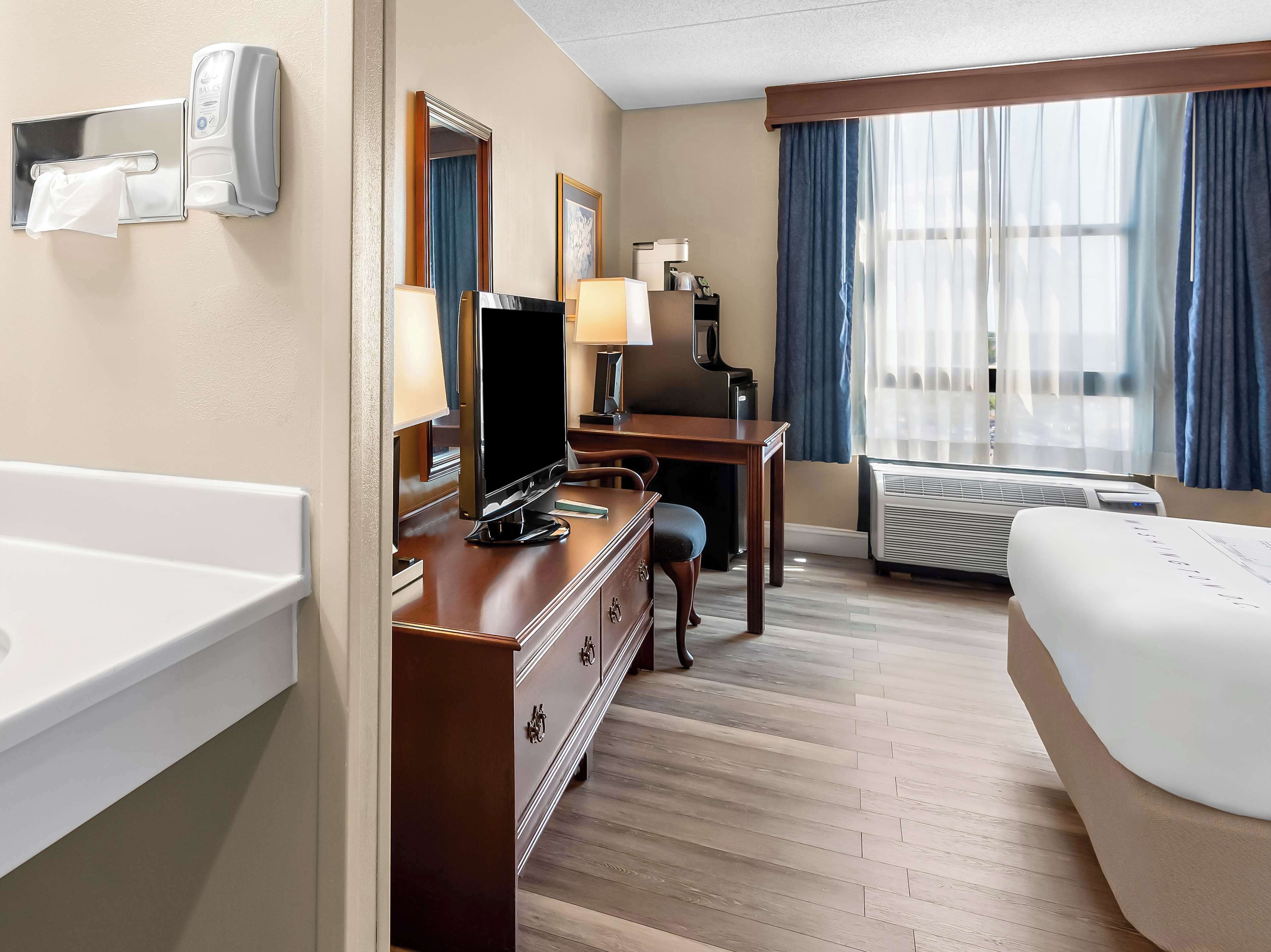 A hotel room with a desk, chair, television, and a bed.