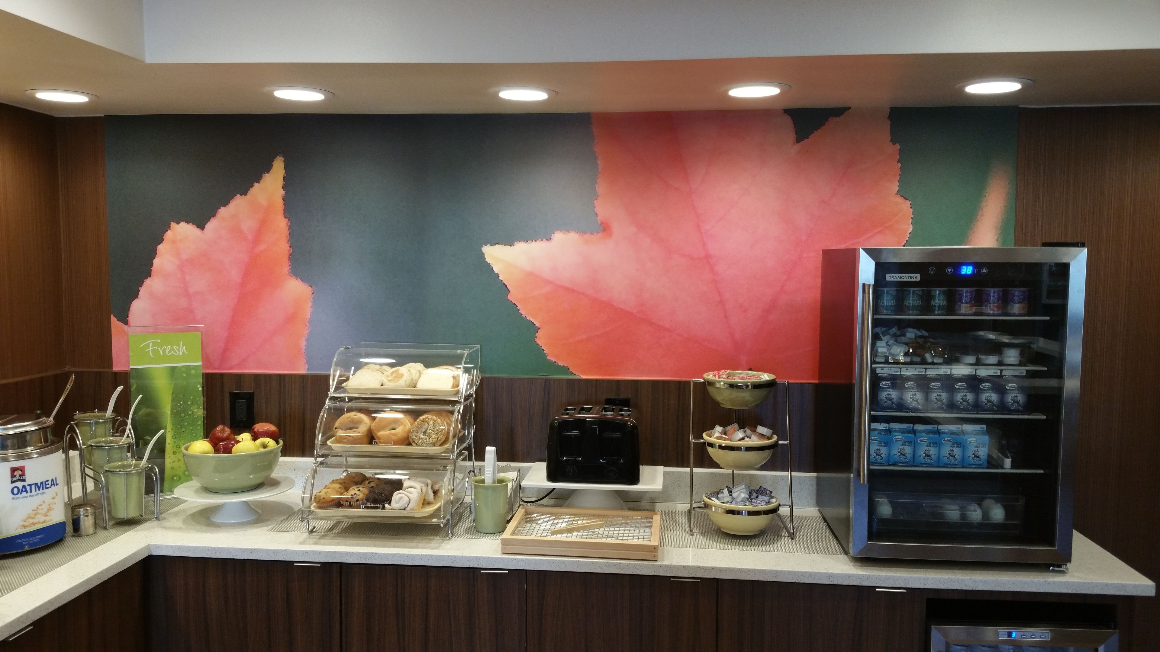 A breakfast bar with various food items, a refrigerator with beverages, and a wall with a leaf design.