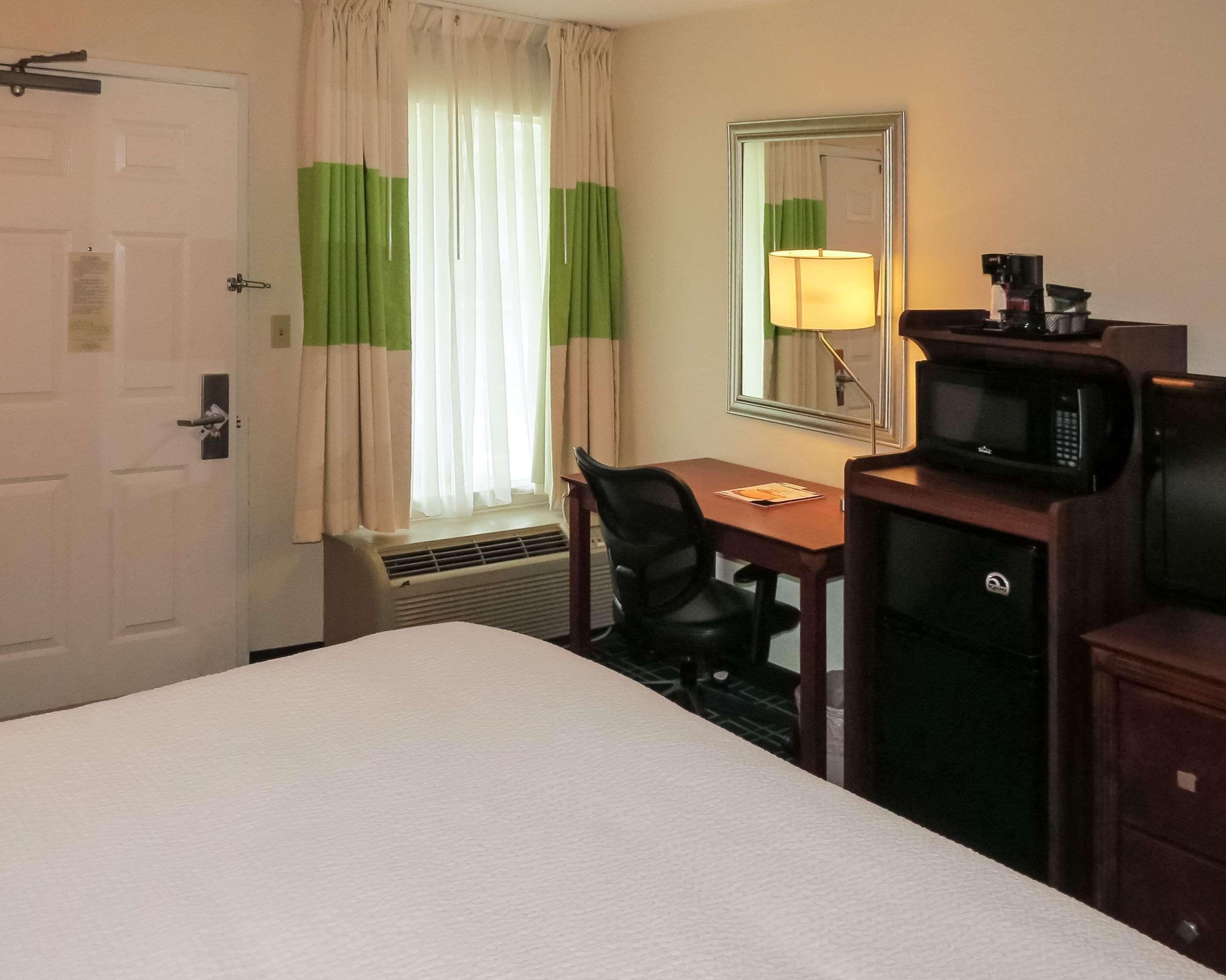 A hotel room with a bed, a desk with a chair, a microwave, and a mirror on the wall.
