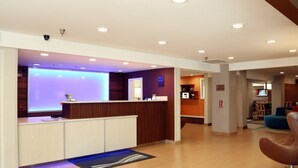 A modern hotel lobby with a reception desk, a blue-lit wall, a wooden reception area, a blue sofa, and a brown chair. - Quality Inn Cranberry Township (Cranberry Township)