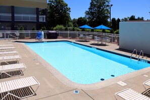 Une piscine rectangulaire avec une terrasse blanche, entourée de chaises longues et de parasols.