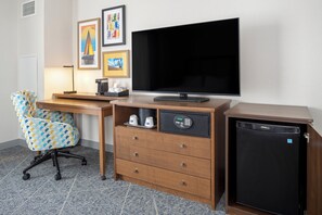 Una habitación de hotel con escritorio, silla, televisión y un refrigerador pequeño.