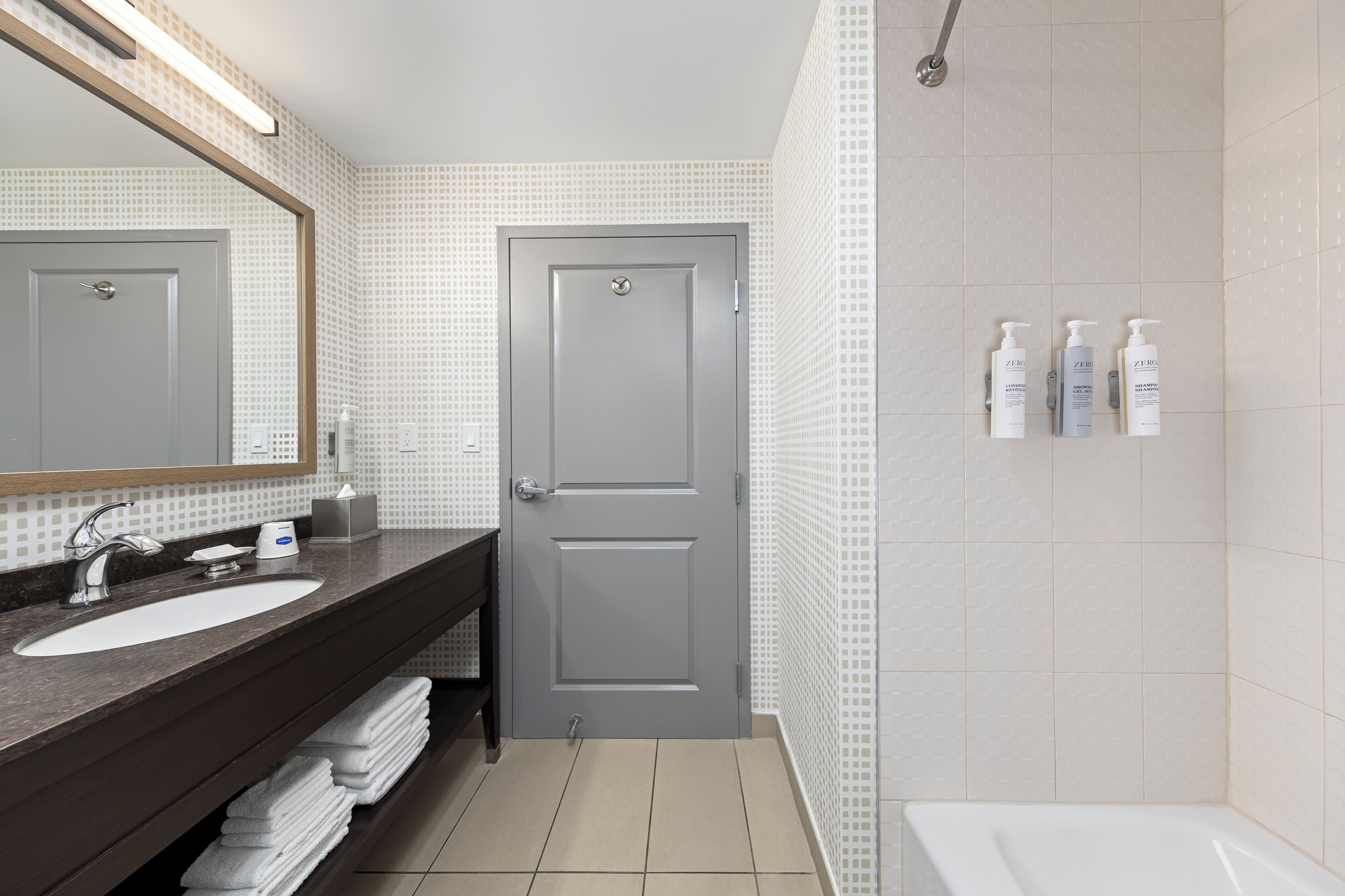 Een moderne badkamer met een grijze deur, een wastafel, een spiegel en een douche.