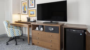 A hotel room with a desk, chair, television, and a mini-fridge.