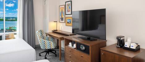 A hotel room with a bed, a desk with a television, a chair, and a coffee maker.