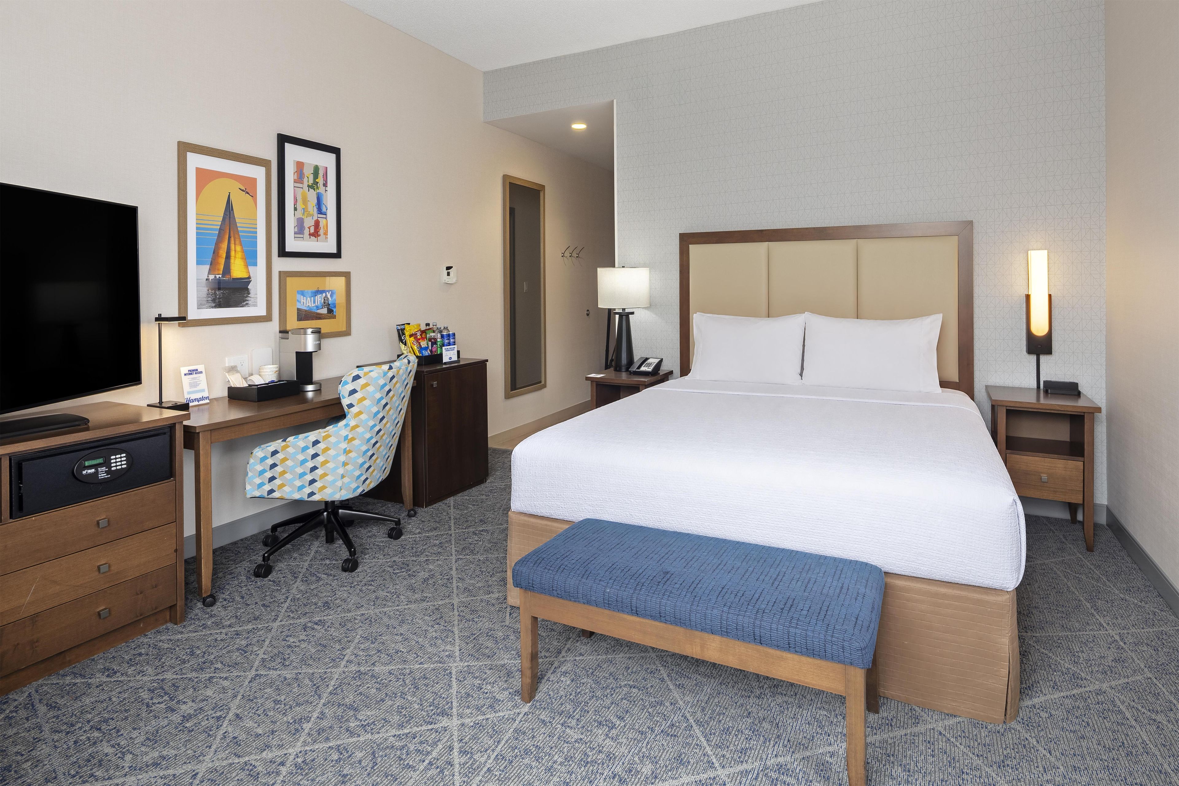 A hotel room with a bed, desk, chair, television, and artwork on the wall.