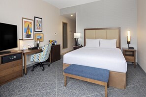 A hotel room with a bed, desk, chair, television, and artwork on the wall.