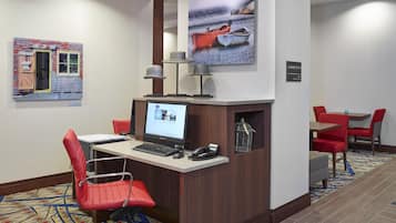 A hotel reception area with a desk, computer, phone, and red chairs.