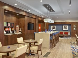 A hotel lobby with a bar area, seating, and a television screen.