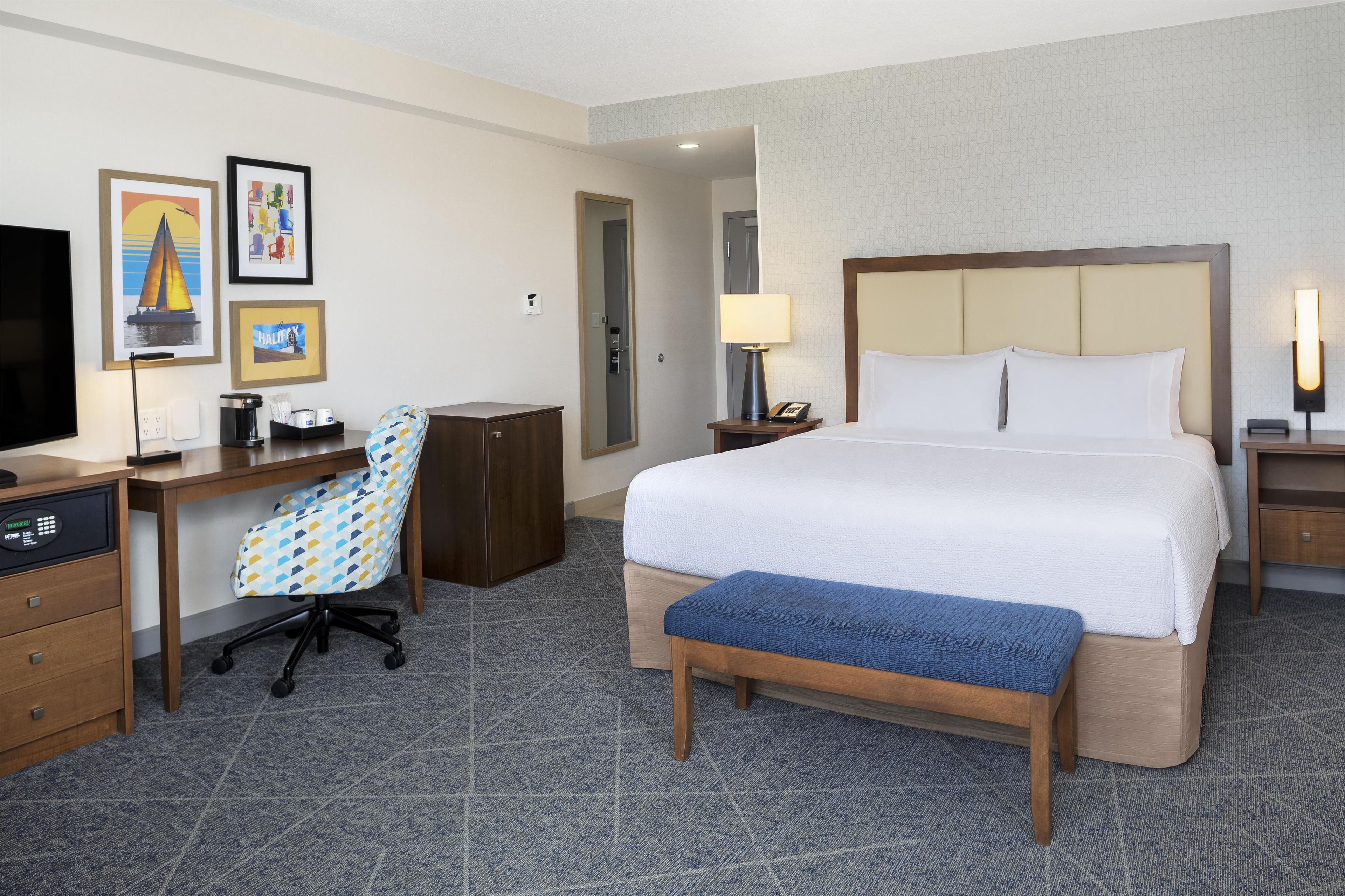 A hotel room with a bed, desk, chair, and a television.