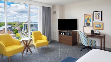 Una habitación de hotel con un ventanal grande, un televisor de pantalla plana, un escritorio con una silla y una cama.