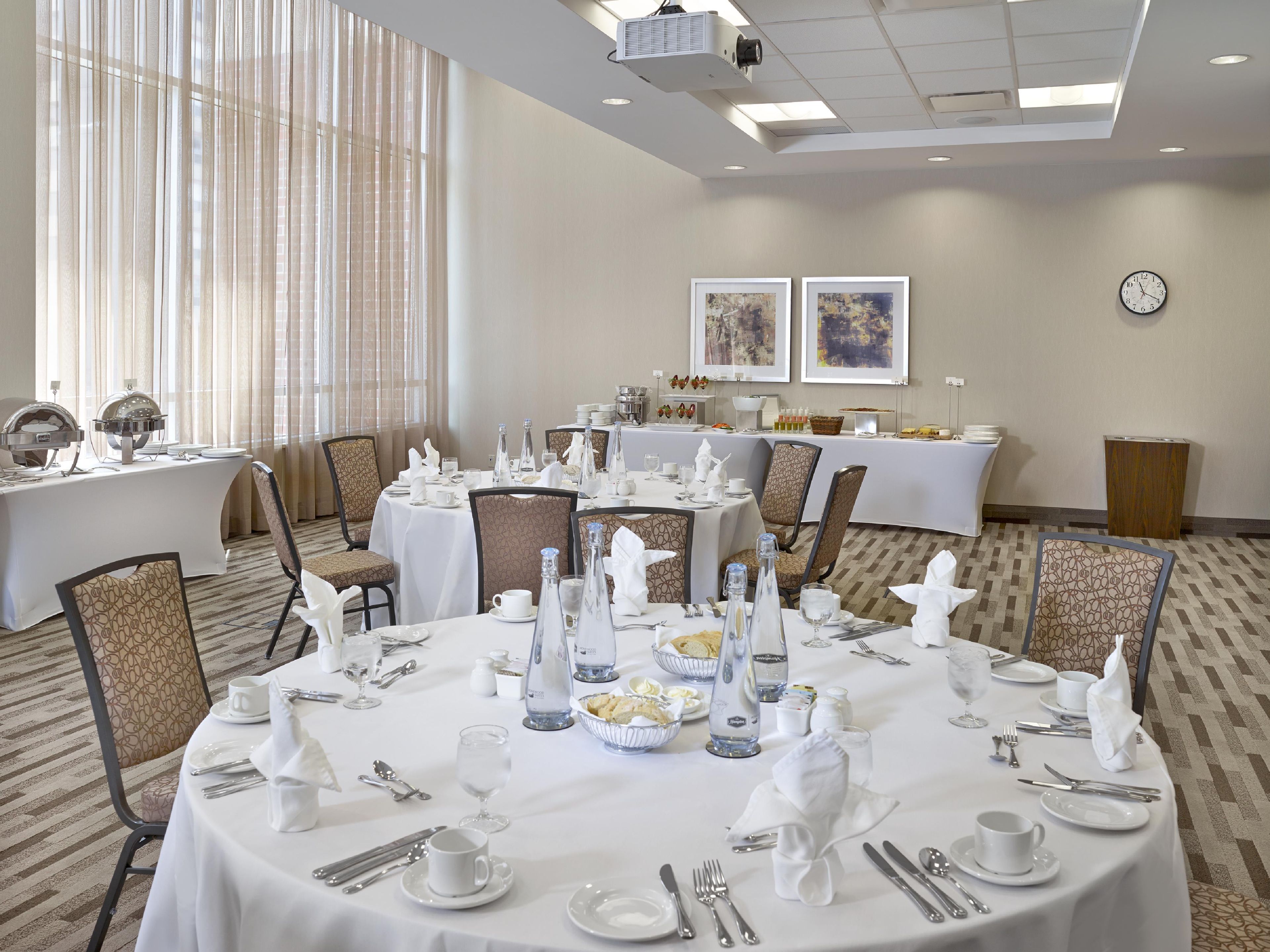 A conference room with round tables set for a meeting, equipped with nameplates, water bottles, and a projector on the ceiling.