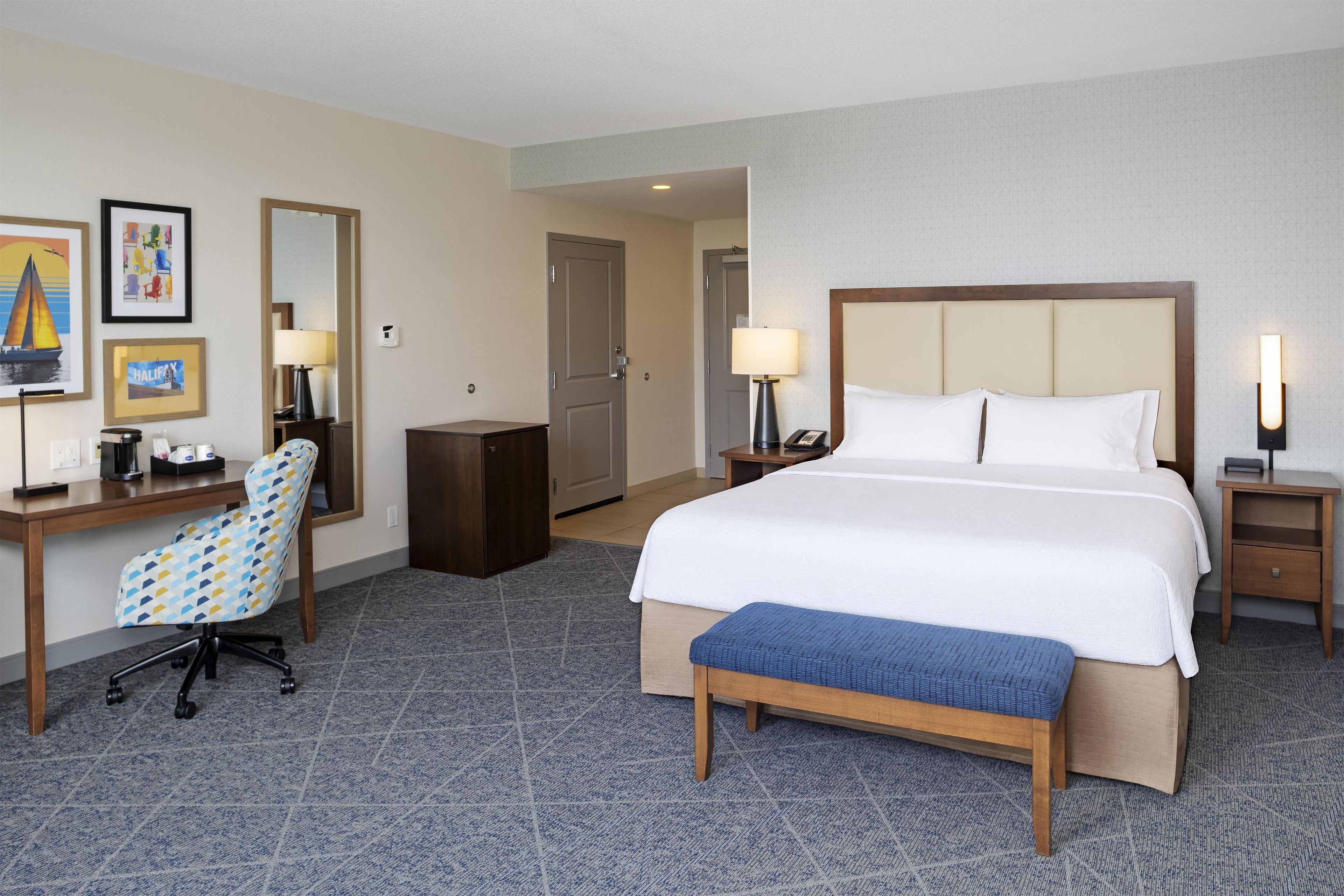 A hotel room with a bed, bedside tables, a desk, a chair, and a bench.