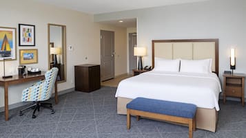 A hotel room with a bed, bedside tables, a desk, a chair, and a bench.