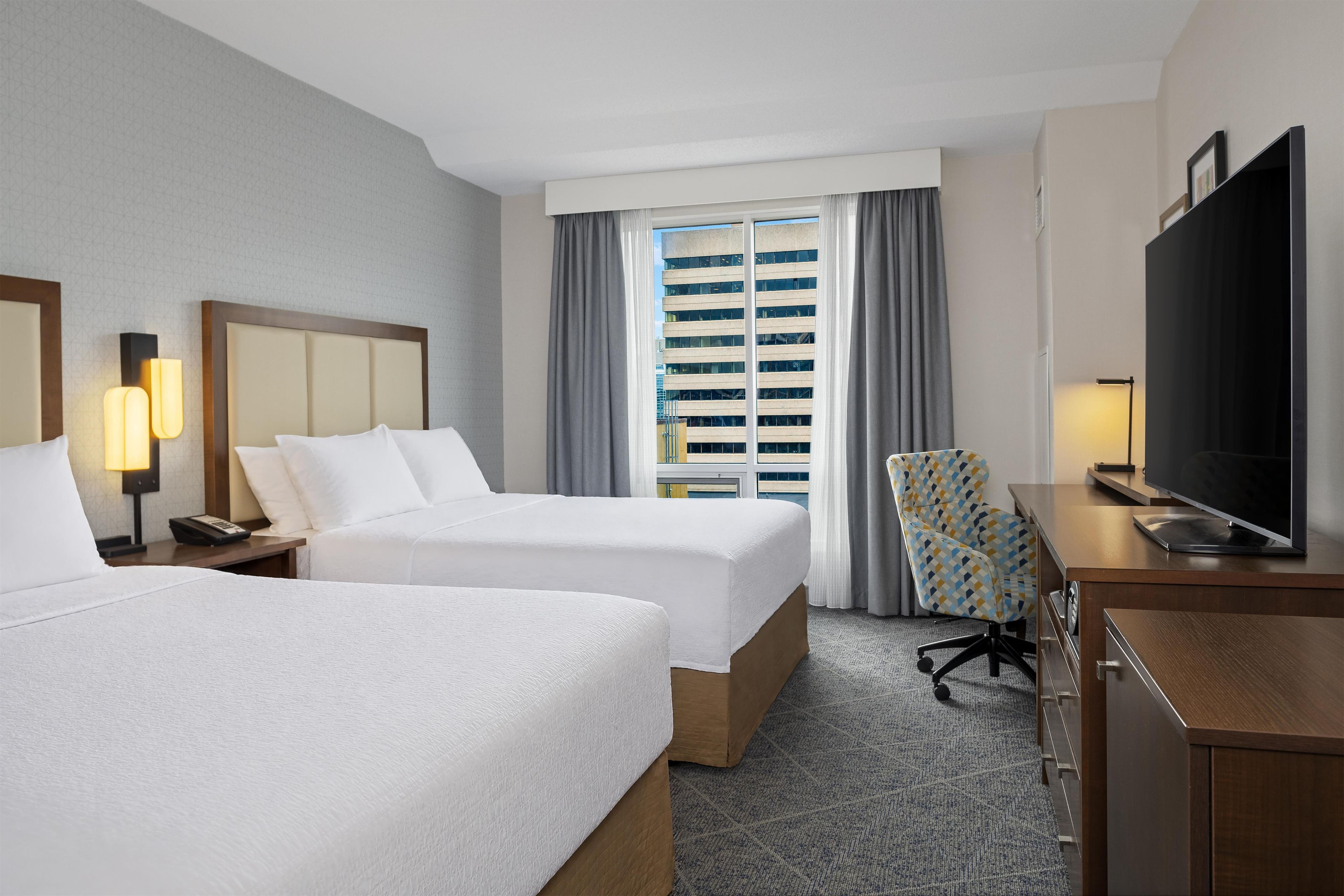 A hotel room with two beds, a desk with a television, and a chair.