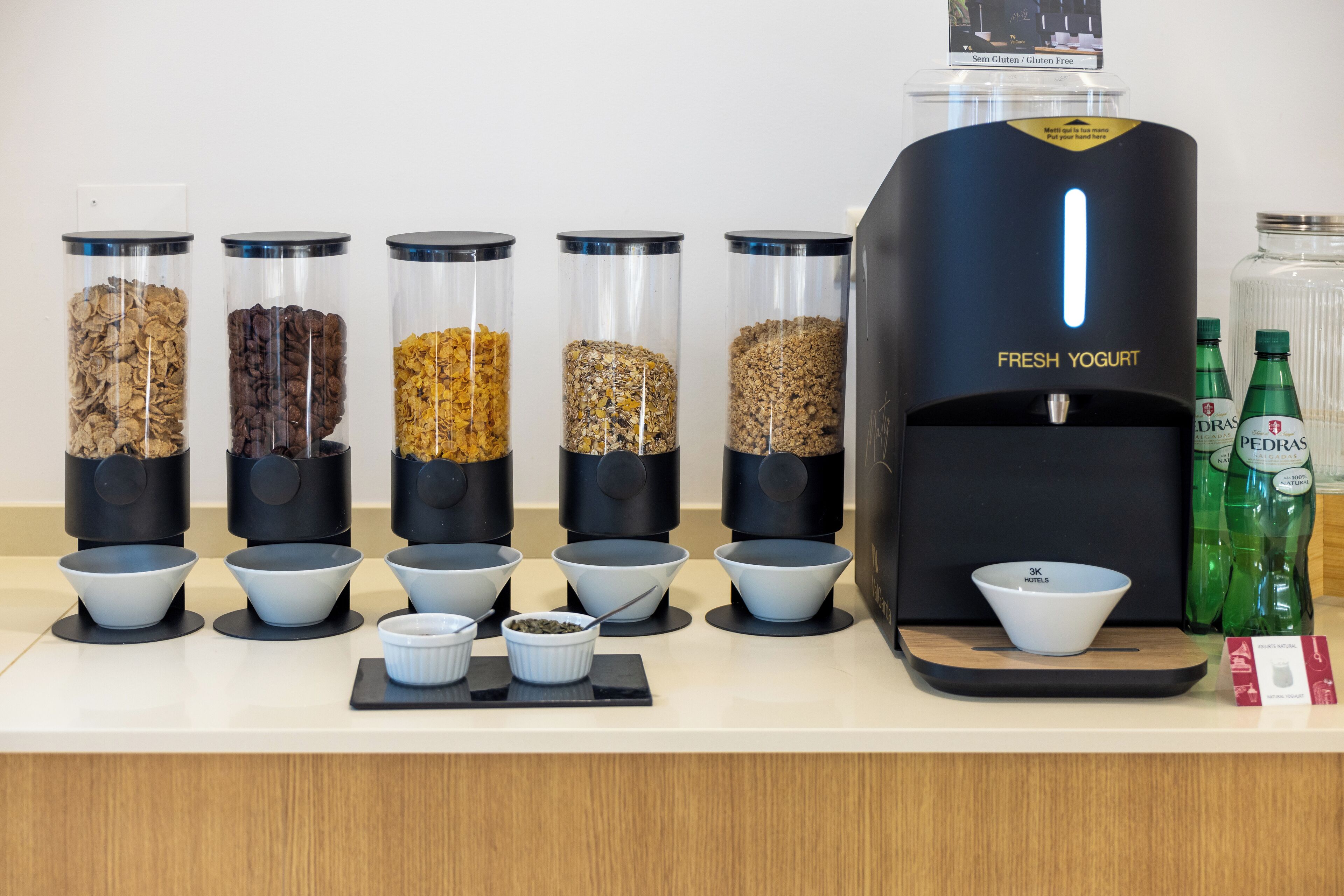 A yogurt dispenser with multiple containers of different toppings and a selection of bottled beverages.