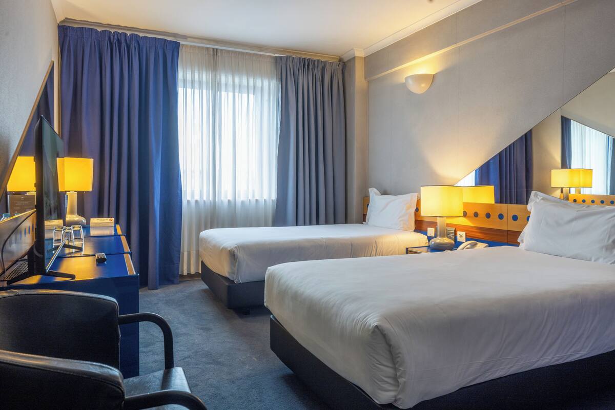 Ein Hotelzimmer mit zwei Betten, einem Schreibtisch mit Computer und einem Stuhl.