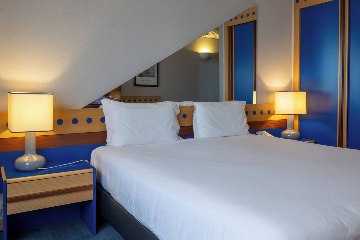 Ein Hotelzimmer mit einem großen Bett, zwei Nachttischen mit Lampen, einem hölzernen Kopfteil und einem Spiegel an der Wand.