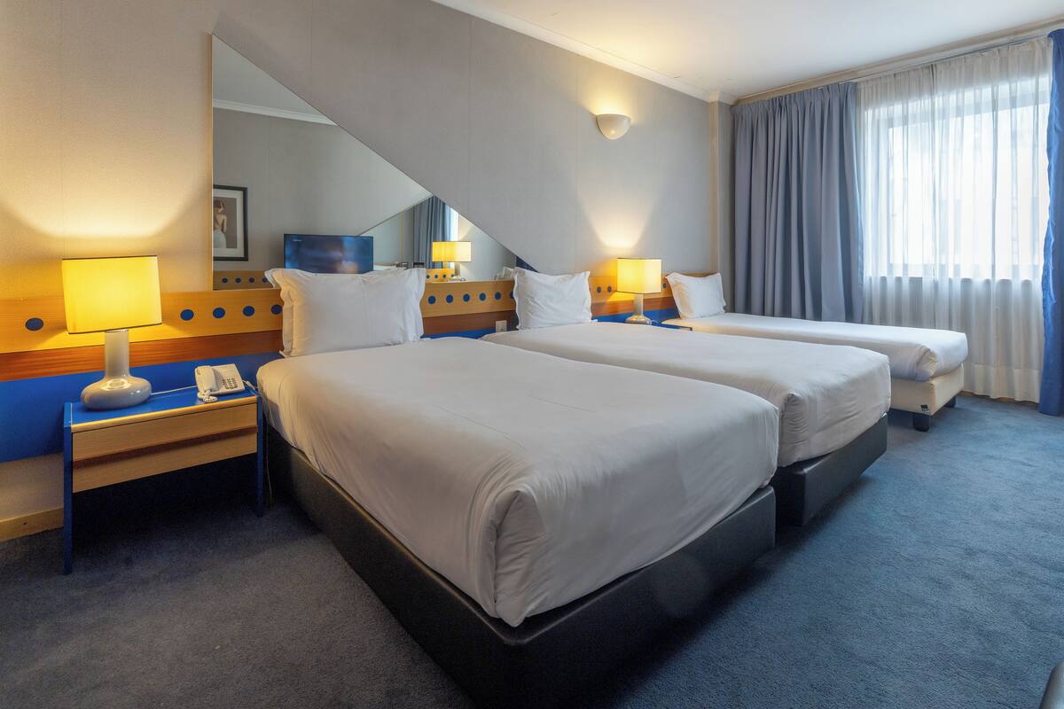 Ein Hotelzimmer mit zwei Betten, einem Schreibtisch, einem Telefon und einem Spiegel.