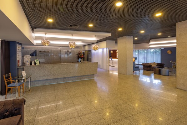 A spacious lobby with a reception desk, seating area, and a large window providing natural light.