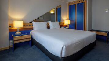 Een hotelkamer met een groot bed, twee nachtkastjes met lampen, een houten hoofdbord en een blauwe accentmuur.