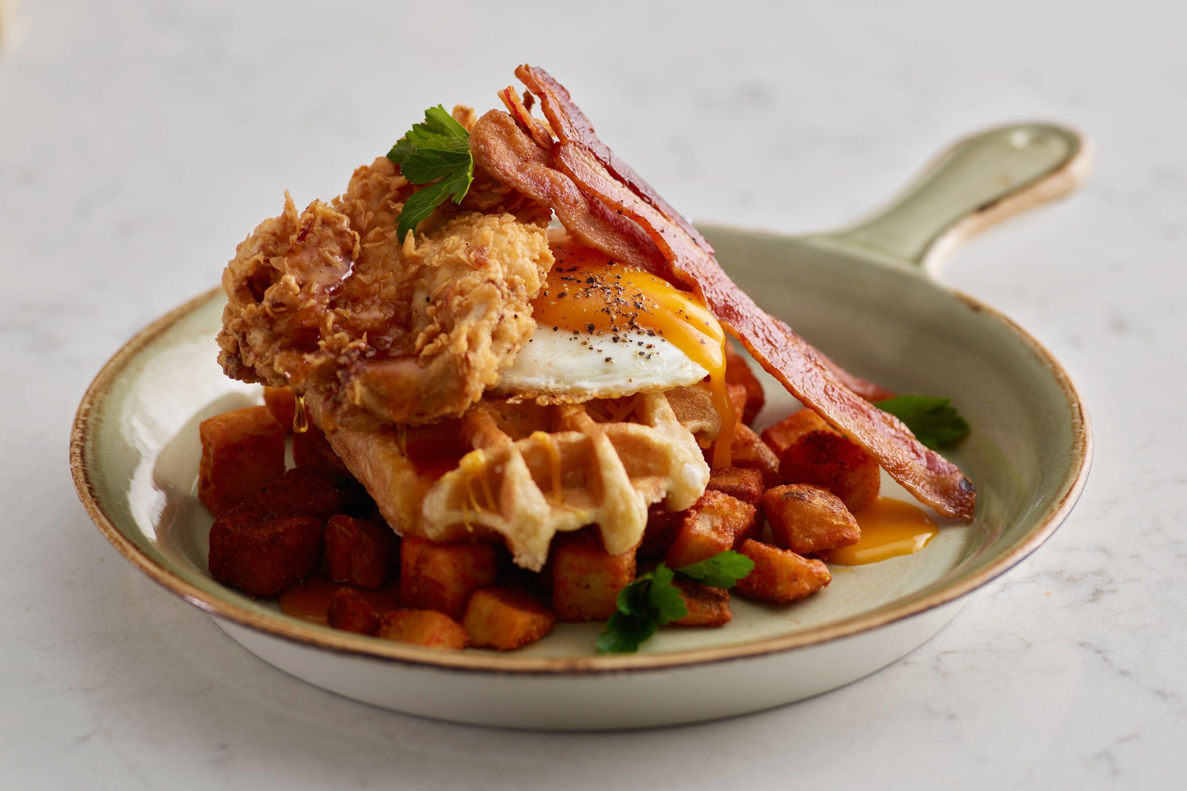 Un plato de comida con pollo frito, tocino, un huevo frito y patatas en cubos.