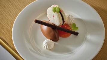 A dessert on a white plate with a chocolate piece, a small green leaf, and a dollop of cream.