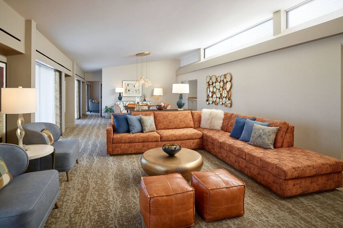 Ein modernes Wohnzimmer mit Ecksofa, Poufs, einem runden Couchtisch und einem Essbereich im Hintergrund.