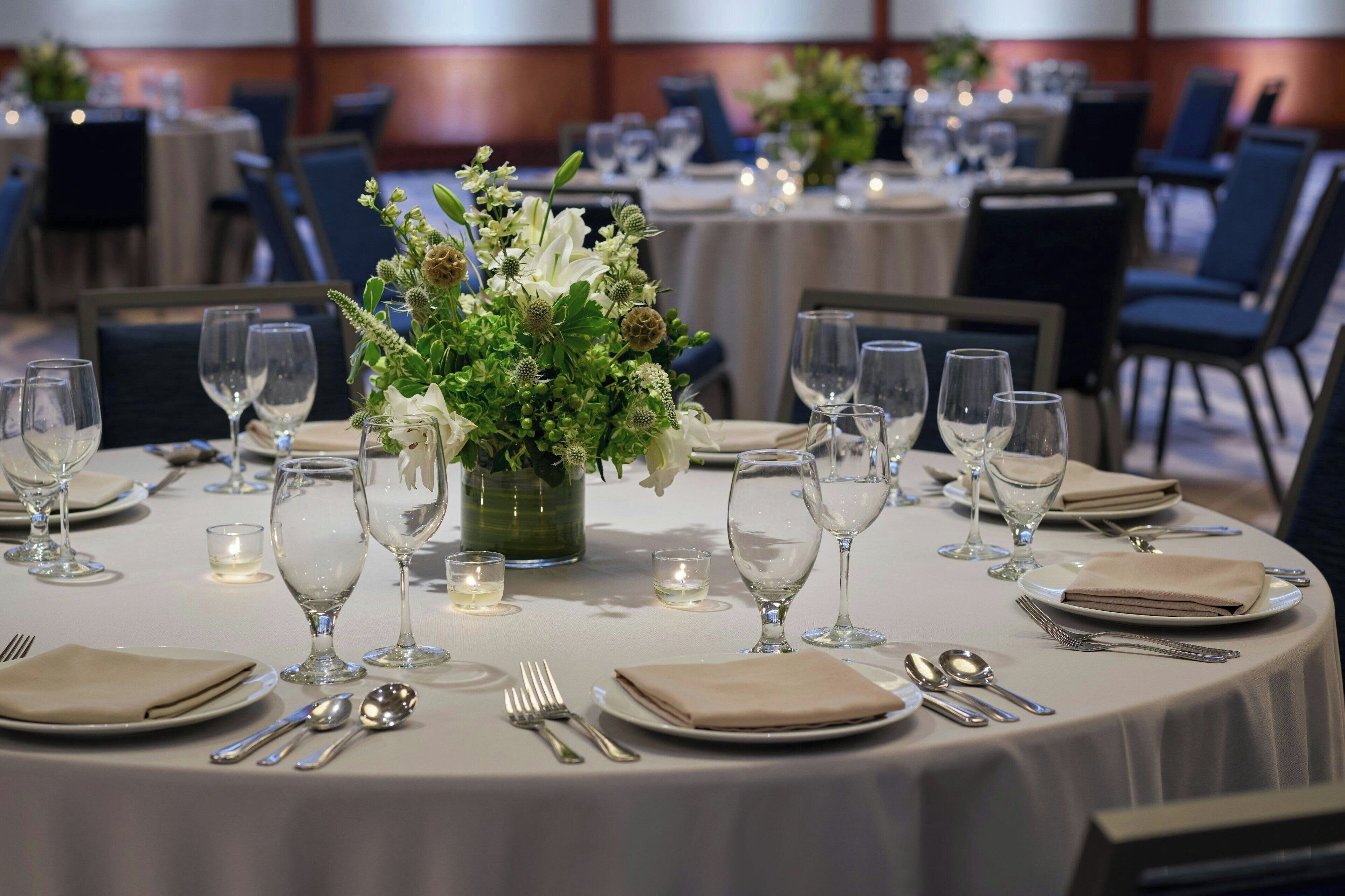 A banquet hall with round tables set for dining, each with a centerpiece of flowers and candles.