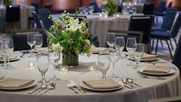 A banquet hall with round tables set for dining, each with a centerpiece of flowers and candles.
