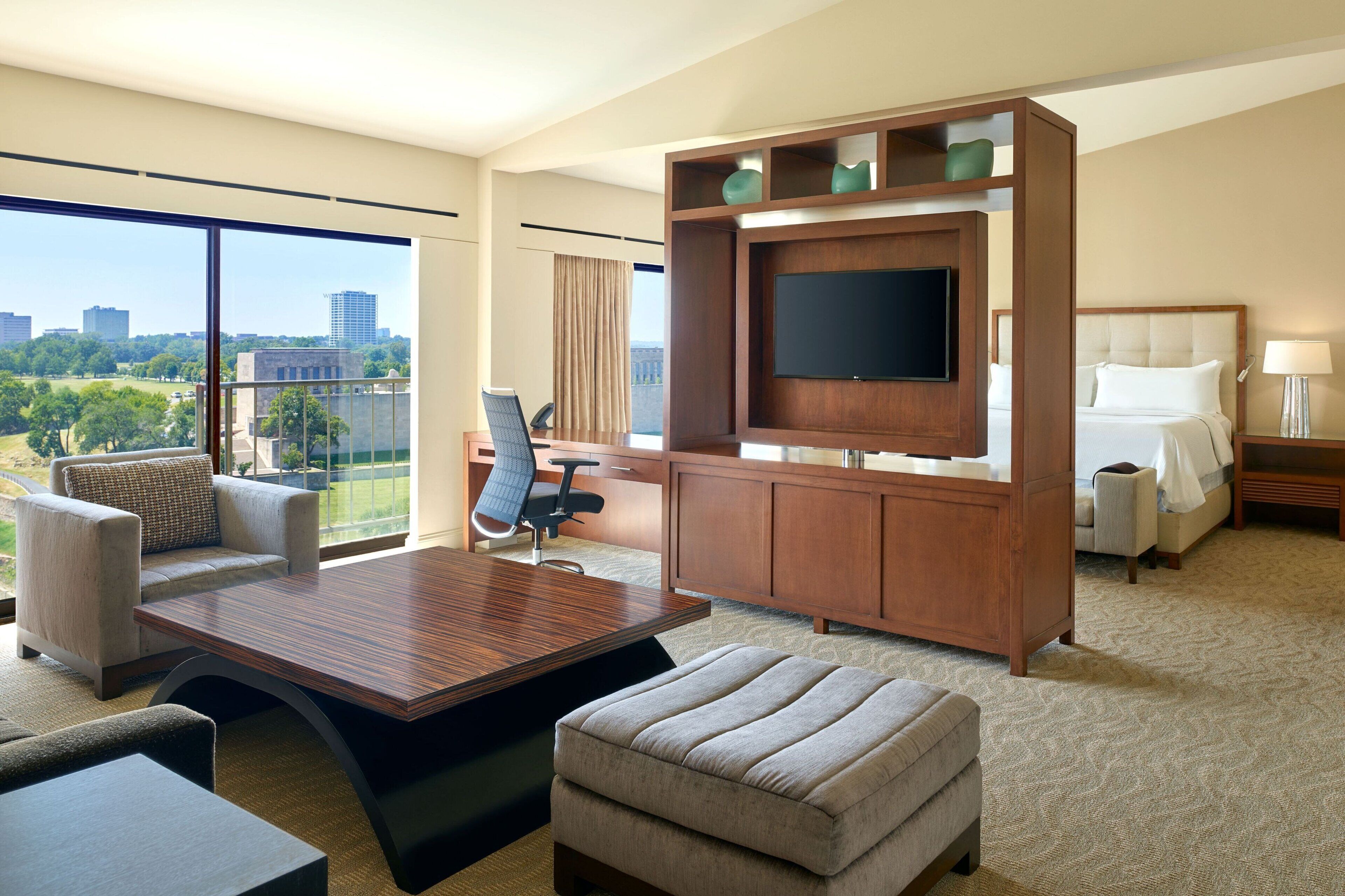 A hotel room with a large window, a flat-screen TV, a sofa, a desk, and a bed.