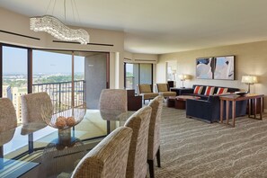 A modern hotel room with a balcony, a dining area with a glass table, and a living area with a sofa and lamps.