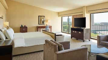 A hotel room with a large bed, a desk with a chair, a television, and a balcony with a view.