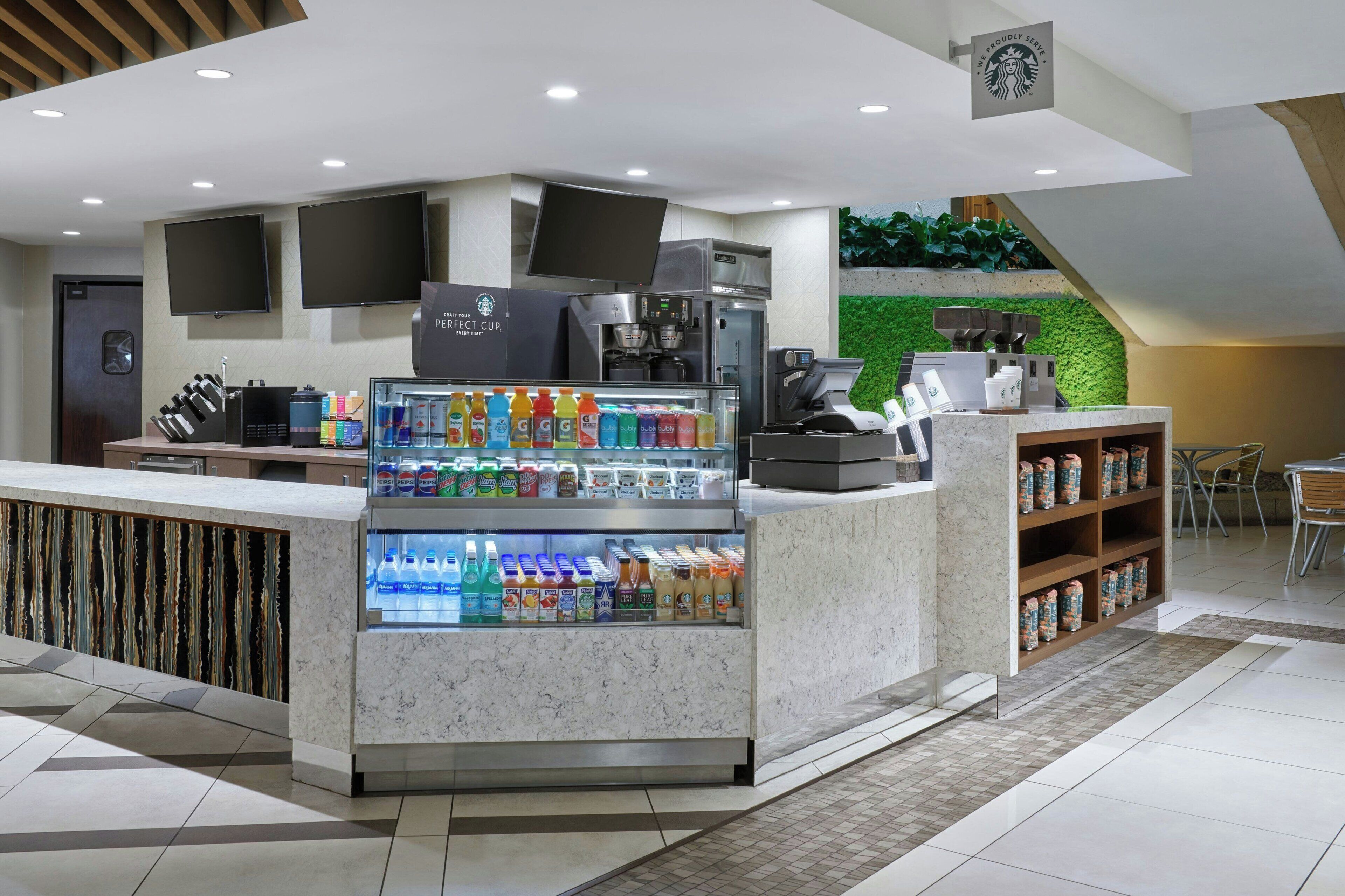 Una cafetería moderna con mostrador de mármol, exhibidor refrigerado de bebidas y una pared verde.